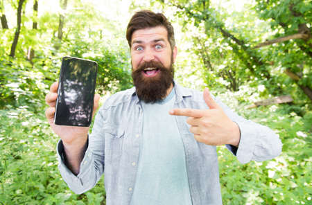 look here. happy bearded man pointing finger on phone. Mature hipster with beard. got lost in forest. brutal man with phone. hipster style. guy in forest use gps navigation. summer campingの写真素材