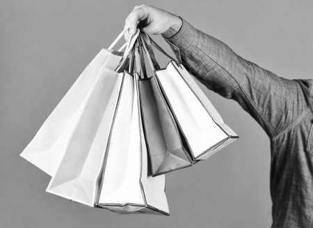 Hand hold bags. Shopping bags in hand on red background. Paper bags different colors. Shopping in mall. Black friday concept. Holidays preparation and celebration. Gift and present. Deliveryの写真素材