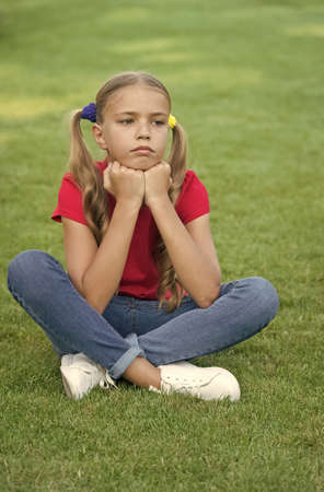 Little girl cute ponytails hairstyle relaxing on green grass, sad day concept