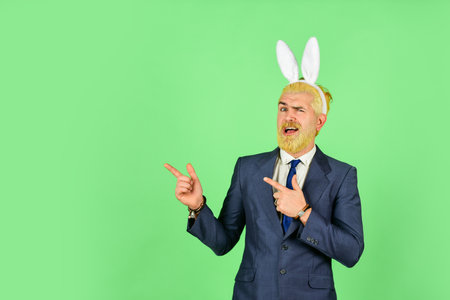 Preparation for holy sunday. Happy manager pointing fingers at something. Bearded man with bunny ears pointing green background. Pointing gesture. Pointing and promoting. Order now, copy spaceの写真素材