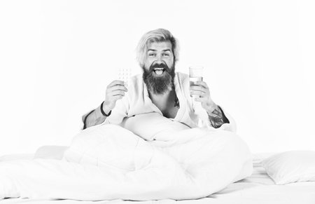 Hangover concept. Man painful face waking up in morning. Hipster drink water take medicines. Headache hangover. Hangover remedy. Missed night of sleep is fairly common experience for young peopleの写真素材