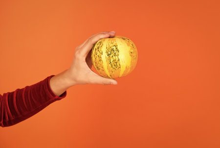 halloween pumpkin in hand of child creating jack o lantern for holiday on orange background, happy halloweenの写真素材