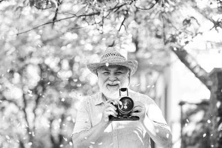 Walking his favorite street. Enjoying free time. Travel and tourism. Travel photo. Photographer in blooming garden. Capturing beauty. Senior man hold camera. Retirement travel. Spring holidaysの写真素材