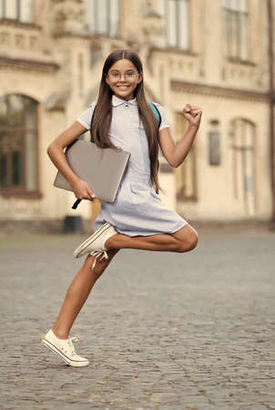 Learning needs change fast. Happy child hurry to school. Little girl carry laptop computer. Modern...