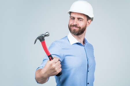 handsome smiling bearded businessman in helmet hold hammer, repairing