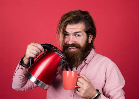 modern technology in life. bearded hipster use home appliances. kitchen concept. brutal handsome man with moustache drink tea. mature man husband hold electric kettle. feeling of surpriseの写真素材