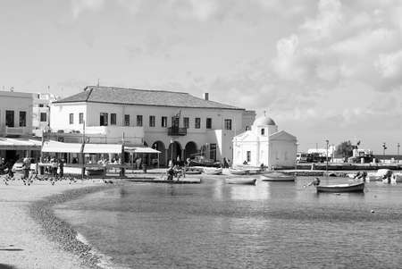Mykonos, Greece - May 04, 2010: church and houses at sea coast. Village at seaside on blue sky. Fishing boats on sea beach. Summer vacation on mediterranean island. Wanderlust and travelling conceptのeditorial素材