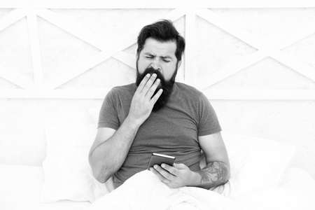 It takes him long to wake up. Sleepy man. Bearded man use mobile phone in bed. Man yawn in morning....