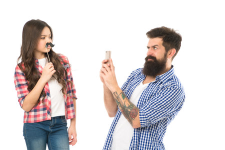 Making family memories. Bearded man take photo of little child. Small girl pose with mustache props. Hipster use mobile phone. Family celebration. Family photo session. Family is everythingの写真素材