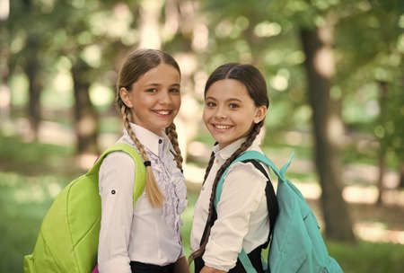 Clever friends. back to school. small school girls walk in spring. happy childrens day. childhood hapiness. two sisters in school uniform outdoor. ready for holidays. happy teen kids carry backpackの写真素材