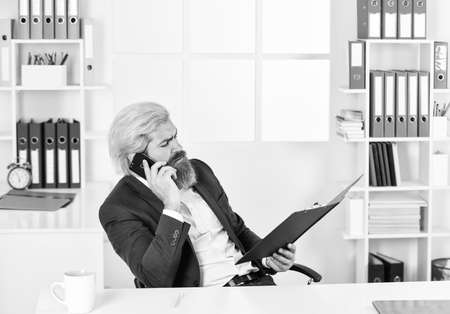 verify data. business management professional. chief information officer speak on phone. smiling IT director or CIO. successful crisis manager make notes in documents. businessman hold office folderの写真素材