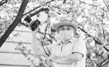 man tourist use camera take photo of cherry blossom. sakura in full bloom photography. senior bearded man in respirator mask. professional photographer work during coronavirus quarantine. spring manの写真素材