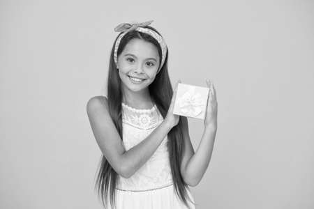 Thank you. Happy child got present. Little child hold gift box. Small child celebrate birthday. Girl child with cute smile yellow background. Enjoying holidayの写真素材