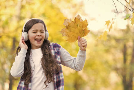 Trendy beauty. childhood happiness. beauty and nature. happy kid wear headphones. teen girl listen music on the way to school. child walk in autumn forest. fall maple leaves in park. online educationの写真素材