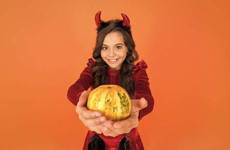 happy halloween devil girl. teenage child in imp horns. cheerful kid carry pumpkin. making jack o...