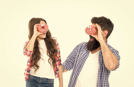 Cheerful family. Sweets and treats concept. Daughter and father eat sweet donuts. Dessert. Happiness and joy. Sweet mood. Bakery shop. Fathers day. Sweet tooth. Girl child and dad hold glazed donutsの写真素材