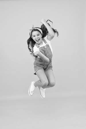 Totally happy. Energy inside. Feeling free. Summer holidays. Jump of happiness. Small girl jump yellow background. Enjoy freedom. Childrens day concept. Spirit of freedom. Active girl feel freedomの写真素材