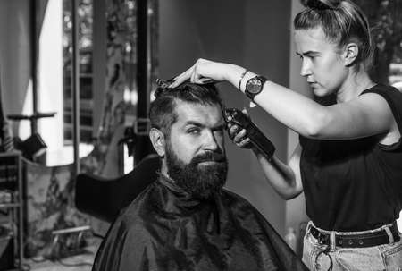 male barber care. bearded man at hairdresser chair in salon. beauty and fashion. hair and beard styling. brutal guy with barbershop professional master use electric shaver. Cool and confidentの写真素材