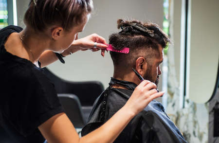 shot of hairdresser cutting hair of handsome man client, Hairstylist serving client at barber shopの写真素材