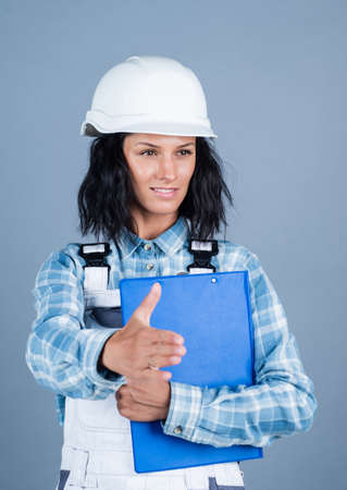greeting or welcome. girl in workshop uniform. engineering. architect working with folder. female foreman on construction site. carpenter assistant wear protective helmetの写真素材