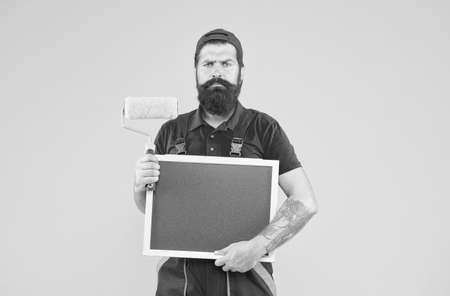 mature bearded guy painter worker in boiler suit uniform using paint roller tool for painting wall...