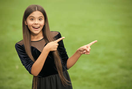Look at this. Happy girl point index fingers green grass. Objective pointing. Hand gesture. Marketing product or service. Indicating event or location. Pointing for copy spaceの写真素材