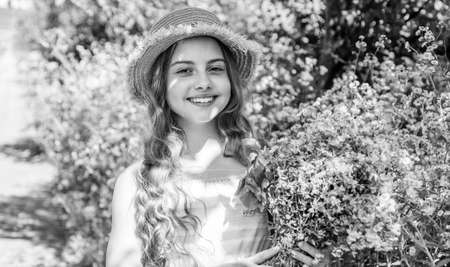 Happy small girl with sun hat on long hair smile with flowers on sunny summer landscape, march 8の写真素材