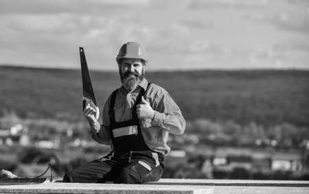 Construction carpentry. Man builder wear uniform and hard hat for protection. Carpentry concept. Hard labour on sunny day outdoors. Bearded construction worker. General construction experienceの写真素材