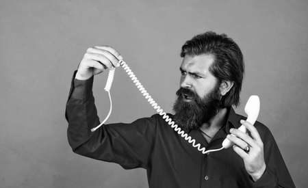 mature male hold broken retro phone. guy with beard and moustache answering the call. telephone conversation. bearded man. communication in modern life. speak with friend on phoneの写真素材