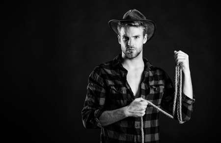 Lasso tool of American cowboy. Still used on ranches to capture cattle or other livestock. Western life. Man unshaven cowboy black background. Cowboy wearing hat hold rope. Lassoing on prairieの写真素材