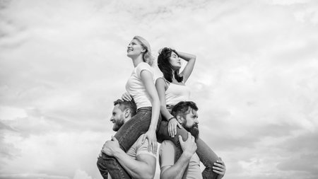 Enjoying themselves. Happy men piggybacking their girlfriends. Loving couples enjoy fun together. Loving couples having fun activities outdoor. Playful couples in love smiling on cloudy skyの写真素材