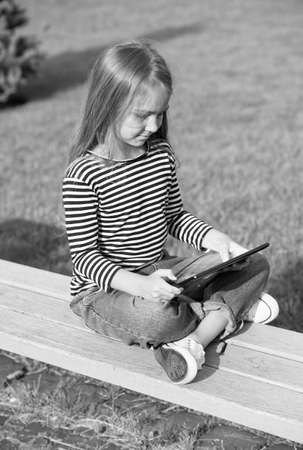 Experience changing the way you learn and play. Small child use tablet sitting on park bench. Mobile technology. Modern life. New technology. Online school and homeschooling. Distance educationの写真素材