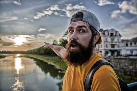 Guy in front of blue sky at evening time admire landscape. Enjoy pleasant moment. Man in cap enjoy sunset while stand on bridge. Take moment to admire sunset nature beauty. River sun reflectionの写真素材