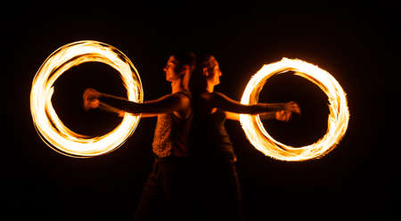 Creating awesome tracer effects. Couple of artists perform fire orbitals. Bright light trails and designs. Fire performance. Burning poi twirling. Night festival. Holiday celebrationの写真素材