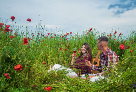 man and woman having romantic date in poppy flower field with guitar music and wine, loveの写真素材