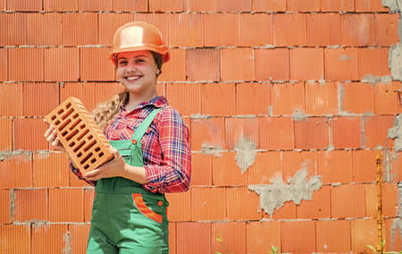 teen girl hold brick. little builder with brick. child is engineer architect. building her future house. happy childhood. kid wear protective helmet. protect head on construction siteの写真素材