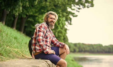 Nice day. Rest and relax. Relaxation and pleasure. Bearded hipster relax outdoors. Man tourist sit riverside. Man with beard and moustache relaxing nature background. Tourism concept. Summer vacationの写真素材