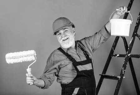 Painter working at construction site. senior man use roller on ladder. work in apartment. Craftsman With Paint Roller. House Painting and Renovation Business. making repair tool. Safety expertの写真素材