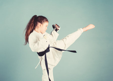 Karate gives feeling of confidence. Strong and confident kid. She is dangerous. Girl little child in white kimono with belt. Karate fighter ready to fight. Karate sport concept. Self defence skillsの写真素材