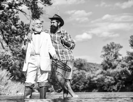 Gone Fishing. Fly fishing adventures. retired father and mature son with beard. friends men with fishing rod and net. happy fishermen in water. hobby of businessman. retirement fisheryの写真素材