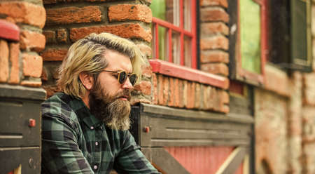 Bearded man checkered shirt. Hipster dyed hair and beard. Hairdresser and barbershop. Brutal male with blond hair irish architecture background. Man casual fashion. Hipster in sunglasses. Cool guyの写真素材