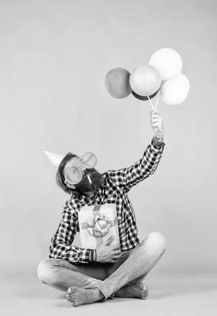 Caucasian mature hipster with funny party glasses in checkered shirt holding balloons and gift box, celebrationの写真素材