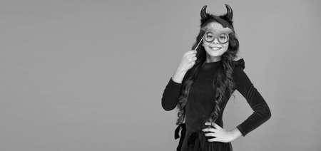 smiling cheerful child in imp horn costume to halloween with bat party glasses, happy halloween, copy spaceの写真素材