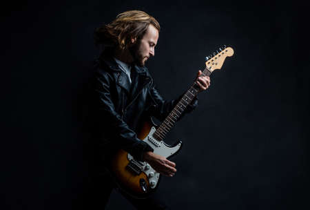 emotional bearded rock musician playing electric guitar in leather jacket and jumping, musicの写真素材