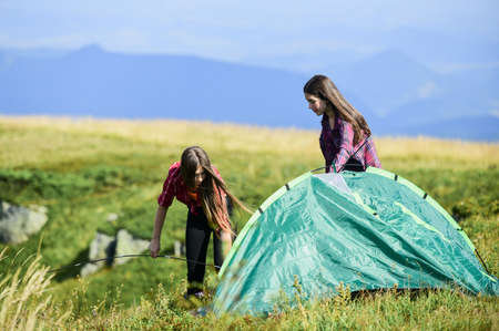 Hiking activity. Attach necessary structural components tent. Helpful to have partner for raising tent. Prepare for night. Girl scout concept. Women set up tent on top mountain. Camping hikingの写真素材