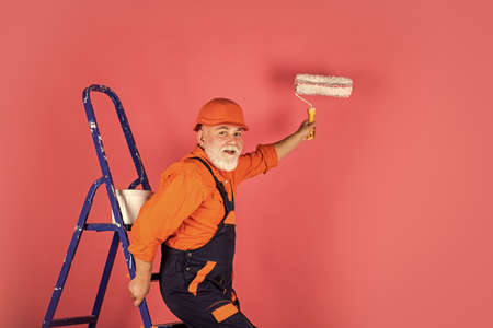 exploring tools. senior man painter use roller on ladder. painting the wall in pink. professional...