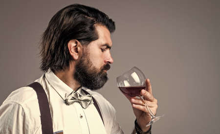 Alcohol use is life abuse. handsome hipster drinking wine glass. sommelier tasting alcohol. bearded man in suspenders drink red wine. brutal guy bartender in bow tie. elegant male barman. copy spaceの写真素材
