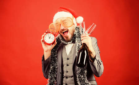 Cheers concept. Join office party. Winter party ideas. Almost midnight. Time to celebrate new year. Christmas party. Man bearded hipster santa hat champagne bottle. alarm clock. Corporate partyの写真素材