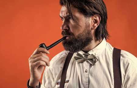 charisma. confident and elegant man in classical wear smoke pipe. masculinity and charisma. formal male smokier. old fashioned bearded hipster smoking pipe. trendy man in suspenders and bow tieの写真素材