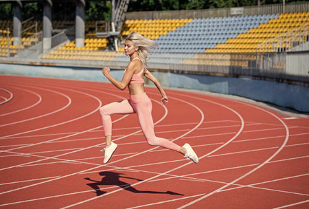athletic lady run on stadium running track. female athlete ready for sprint sport workout. trainer or coach training. marathon. energetic and sporty. sexy fitness woman in sportswearの写真素材